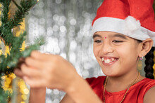Happy Smiling Girl Kid In Santa Hat Decorating Christmas Tree For Festive Holyday Celebration At Home.