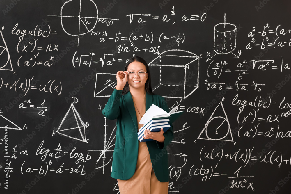 Asian female teacher near blackboard in classroom