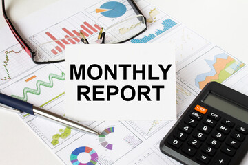 White card with text Monthly report it is lies on financial charts with a calculator and eyeglasses