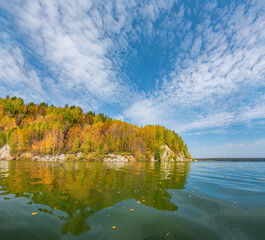 Wall Mural - calm lake, river stone hill on the bank of the river, autumn colored coniferous trees on the other s