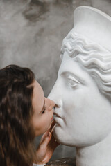 Beautiful curly girl kissing a white plaster head