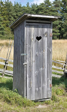 Cute Little Wooden Rustic Outhouse With Carved Heart Shape On The Door. Typical Countryside Vacation Home Toilet.
