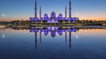 Wall Mural - Sheikh Zayed Grand Mosque in Abu Dhabi day to night transition timelapse after sunset, UAE. Evening view from Wahat Al Karama with reflections on water