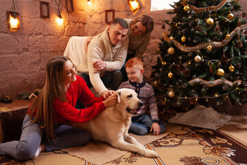 Wall Mural - A happy family of four and a dog celebrate the New Year. Dad, mom, son and daughter love the dog and have fun against the Christmas tree. Labrador and kids.