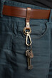 Cropped shot of male body in black shirt and blue jeans with brown belt. Stylish keychain with brown leather belt loop, bronze rings, lobster clasp, charms and keys is fixed on the brown belt. 