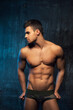Male model in underwear watching to the left. Handsome young man with six pack abs at blue background in studio.