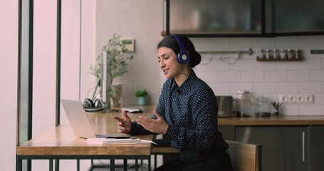 Sticker - Remote job interview, communication using modern wireless technology concept. Indian woman sit at bar counter in kitchen wear headphones looks at laptop screen talk to client or trainee by video call