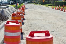 Orange Traffic Barrels And Cones Delineate Road Improvement Curb Construction With Uneven Asphalt Pavement In Residential Neighborhood.