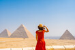 A tourist girl in a red dress looking at the Pyramids of Giza, the oldest Funerary monument in the world. In the city of Cairo, Egypt