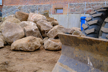 on  building site there is a big pile of field stones and next to it is an excavator