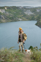 Poster - Female backpacker in warm casualwear with her pet standing against riverside