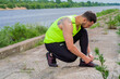 © Georgii - Sportive young guy runner in stylish modern sportswear tying shoelaces before training outdoor