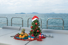 Spruce Tree Decorated With Toys On A Luxury Yacht. Christmas In Tropical Countries. A Plate With Fresh Fruits: Tangerines, Pineapples, Grapes.