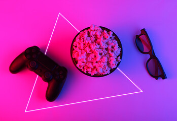 Wall Mural - Gamepads, tv remote, 3d glasses and a bowl of popcorn. Neon pink blue light. Gaming, leisure and entertainment concept. Top view