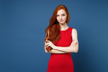 Wall Mural - Smiling confident attractive young redhead woman 20s wearing bright red elegant evening dress standing holding hands crossed looking camera isolated on blue color wall background studio portrait.