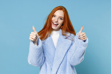 Wall Mural - Excited cheerful funny laughing cute beautiful young redhead woman 20s wearing warm fur coat standing showing thumbs up looking camera isolated on pastel blue color wall background studio portrait.