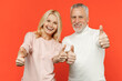 © ViDi Studio - Smiling cheerful funny couple two friends elderly gray-haired man blonde woman wearing white pink casual clothes standing showing thumbs up isolated on bright orange color background studio portrait.