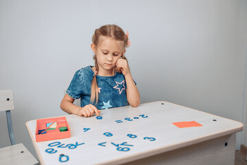 Portrait of a smart pretty girl sitting at a white table drawing and raising her finger up. New idea. Child development. Childhood concept. photo with noise