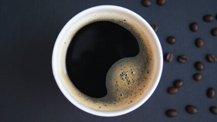 Disposable red cup with fresh hot black coffee and roasted beans on a black background. The concept of coffee to go