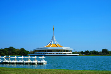 The building with sharp dome on top over a big pond behind water wheel boats under clear blue sky at the Royal King IX Garden 1