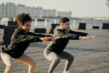 Young sports couple friends are actively engaged in fitness aerobics in the morning. they lead a healthy lifestyle. do stretching exercises in the city. two sportmen coaches a woman and a man.