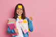 © WHstudio Leushin N - Positive female office worker with folders and stickers wears round glasses and blue jumper points away on copy space gives recommendation how to prepare successful project makes presentation