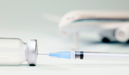 Vaccine in glass vial and syringe with blue cannula, plane in the background