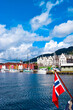 Norwegian flag on the background of the bay and the old wooden houses on the waterfront of Bergen.