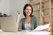 © fizkes - Overjoyed young Caucasian female employee work on laptop in office read good news in paper document. Smiling woman accountant or banker use computer at workplace feel excited with paperwork message.
