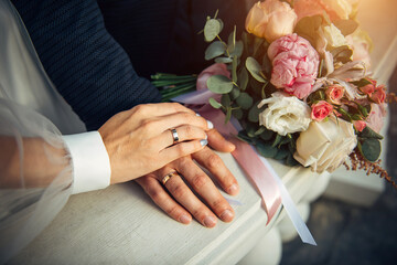 Hands of the bride and groom, wedding bouquet, top view. Gold rings on the fingers of the newlyweds, close-up.