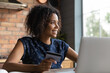 © fizkes - Smiling young african american woman holding plastic bank card in hands, planning products purchase in internet store, looking in distance, dreaming of sale season, planning buying gifts online.
