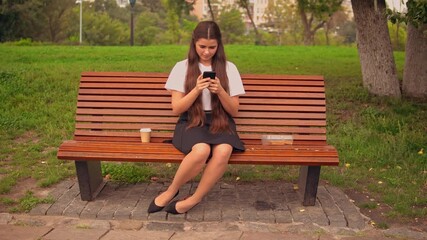 Leinwandbilder - break for lunch student sitting on the bench typing message or scrolling news feed on smartphone drinking coffee to go summer season outdoors
