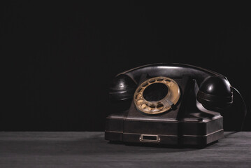 Old retro black rotary phone on the black desk table background with copy space.