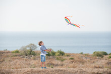 Happy Outdoor Leisure Games By Small Active Caucasian Boy With Flying Kite In Air With Sea Horizon And Blue Sky In Summer