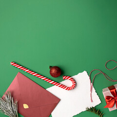 Canvas Print - Christmas layout made with red envelope, card note for copy space, fir branches, candy cane and gift box on green background. Minimal seasonal greeting card concept. Flat lay, top view.