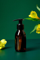 Wall Mural - Amber glass dispenser bottle and flowers on green background. Natural organic cosmetic packaging mockup