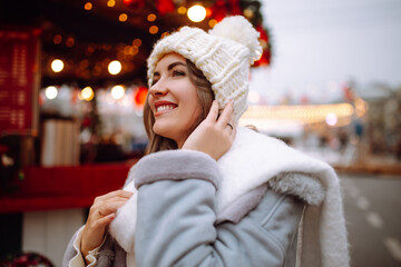 Wall Mural - Beautiful woman enjoys winter holidays walking on Christmas market. Young woman posing on  festive street. New year.