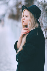 Wall Mural - Stylish beautiful blonde girl in black clothes and hat posing near fence in the street