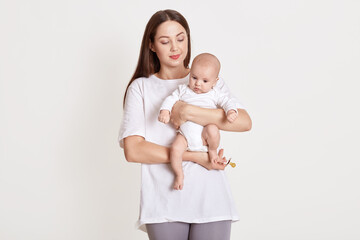 Wall Mural - Closeup portrait of beautiful European woman holding on hands her little daughter on white background. Family, love, lifestyle, motherhood and tender moments.