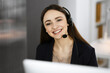 © rogerphoto - Young smiling girl in headsets is talking to the firm's client, while sitting at the desk in a company's office. Portrait of a call center operator at work