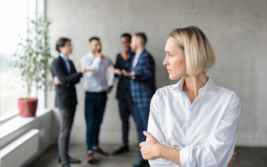 male coworkers whispering behind back of unhappy businesswoman in office