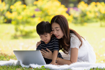 Asian family having fun mother and her son using laptop computer in the park together