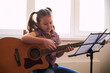 © Максим Корабельщиков - a little girl learns to play the guitar from notes. Music school for children.Musical notation.