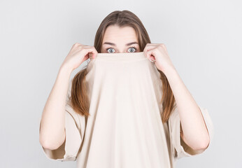 Canvas Print - Close up portrait of surprised woman in white t-shirt covering her face with a t-shirt.