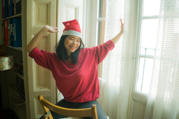 Wall Mural - lifestyle home portrait of young beautiful and happy Asian Korean woman in Santa Claus hat and red jersey enjoying Christmas time smiling cheerful