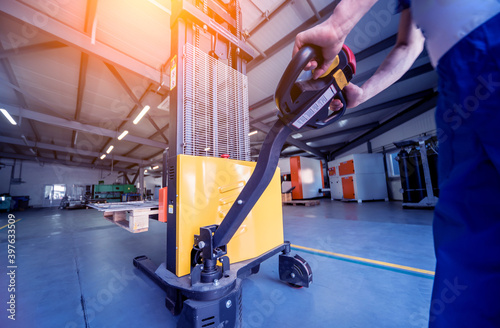 Fototapeta A worker in a warehouse uses a hand pallet stacker to transport pallets