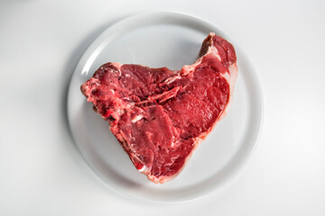 Raw T-bone steak on white round plate