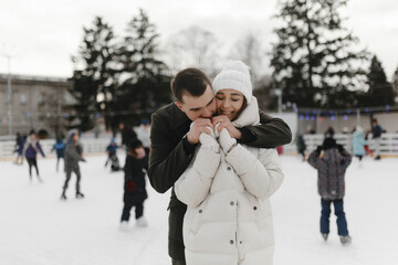 Wall Mural - Man warming hands of the woman in winter. Couple skating on the public skating rink. Winter active date. Love story