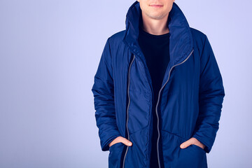  Model in blue down jacket on a blue background. A stern look at the camera and face covered with a down jacket collar. Hands in pockets