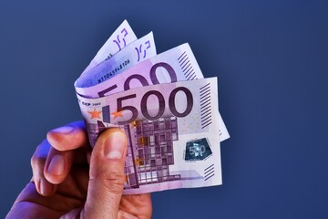 A man hand shows 1000 Euros in two 500 euro banknotes on a blue background